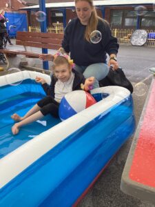 A student enjoys sitting the the paddling pool with bubbles floating across the sky.