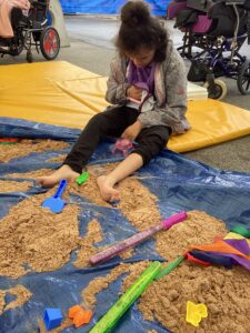 A student enjoys sitting with their feet in the sand.
