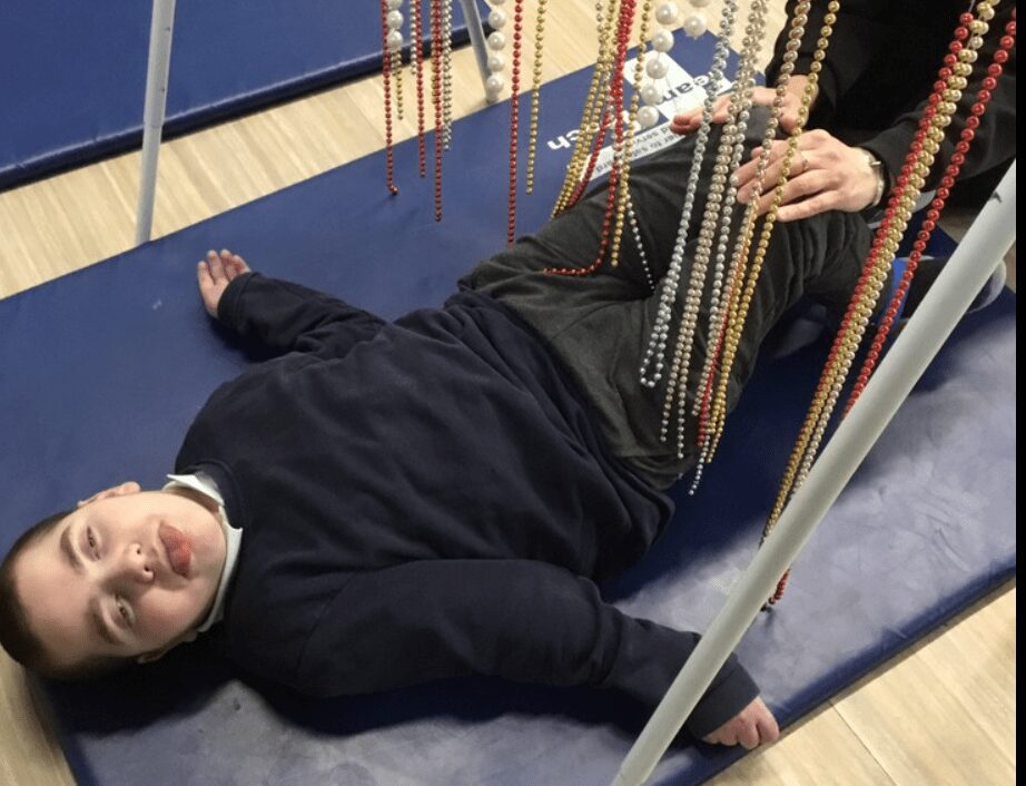 A student lies on their back on a mat beneath some hanging beads.