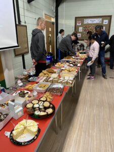 Students help run the cake and coffee stalls. There is a vast array of sweet treats on display.