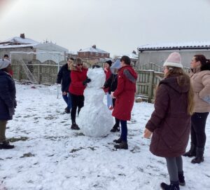 College students are all out in the snow working together to build their snowman.