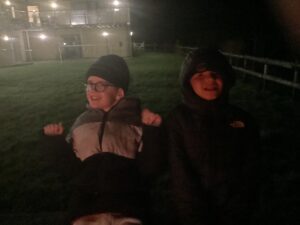 Two students enjoy being out in the dark by sitting by the campfire.