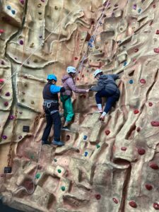 Staff and an instructor assists a student with climbing up the climbing wall.