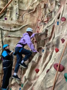 A student begins their journey of climbing up the climbing wall.