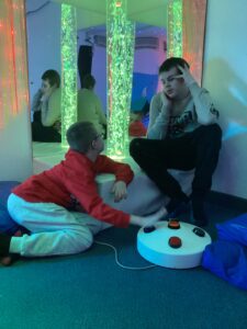 Two students enjoy the sensory room experience. The fibre optics are displaying a variety of colours and the bubble tube is glowing a nice green.