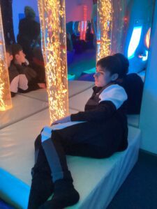 The bubble tube is glowing gold as a student lies and enjoys the sensory experience.