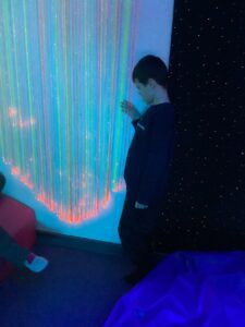 A student enjoys playing with the fibre optic lights that are hanging with lots of colours visible.
