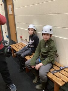 Two students sit on the bench waiting patiently for their turn on the climbing wall.